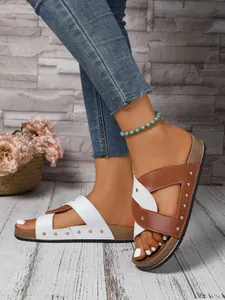 Detail view of stylish women's flat sandals with brown and white rivet cross straps