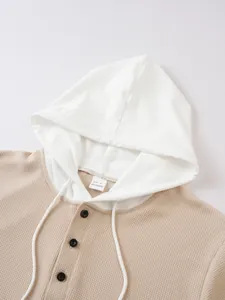 Close-up detail of waffle knit texture, contrast hood, and buttons on men's casual hoodie.