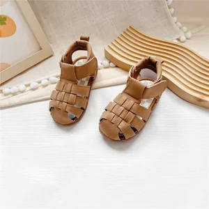 Macro detail view of brown closed-toe leather baby sandals with woven strap design