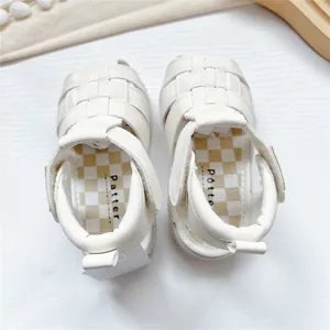 Detailed top view of white woven baby sandals with checkered insole and Velcro strap