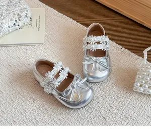 Close-up of silver girls' Mary Jane shoes with floral lace straps and pearl bow detail