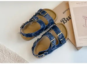 Vista dettagliata di sandali in denim blu per bambini con doppie fibbie e suole marroni.
