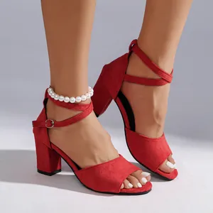 Detail of red suede block heel sandals with cross straps and elegant pearl anklet detail.