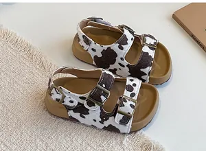 Dettaglio dei sandali da bambina con stampa muccata, fibbie metalliche e suole color cuoio