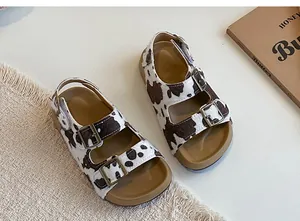 Primo piano di sandali per bambini con stampa mucca e fibbie metalliche su un tappeto.