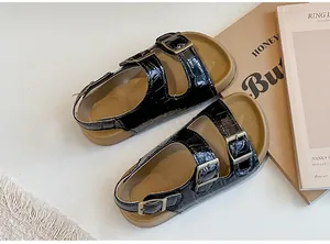 Dettaglio di sandali neri in coccodrillo per bambine con doppie fibbie.