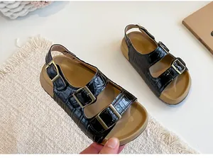 Dettaglio di sandali neri per bambine con motivo a coccodrillo e doppie fibbie eleganti