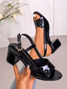 Dettaglio delle eleganti scarpe aperte in pelle verniciata nera con tacco largo e cinturino.