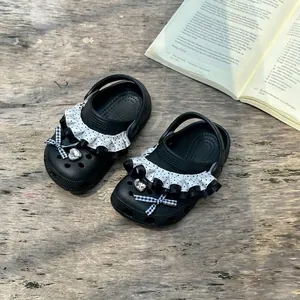 Detailed view of black girls' polka dot clogs featuring ruffles and a heart crystal.