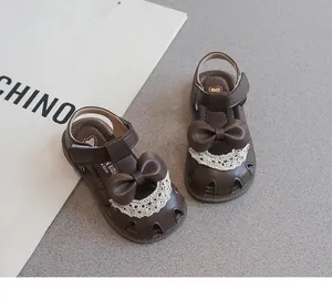 Primer plano de sandalias marrones de niña con lazo y detalles de encaje.