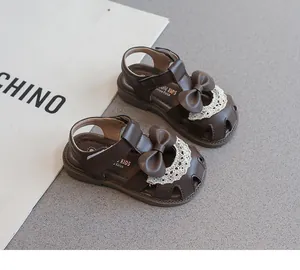 Detalle de sandalias marrones para niña con lazo dulce y ribete de encaje