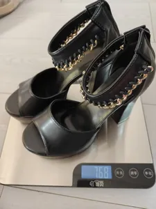 Tacones negros con plataforma y cadenas doradas en una báscula que pesa 768 gramos.