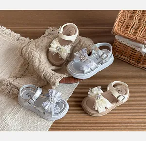 Sandales fille avec nœud strass en argent et crème sur une surface en bois