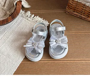 Sandales argentées fille avec nœud en dentelle et fleur en strass sur fond bois