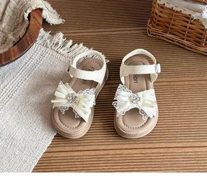 Détail rapproché des sandales crème pour filles avec nœud en dentelle et fleur strass.