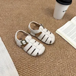 Detalle de sandalias romanas retro de color blanco roto para niños sobre alfombra