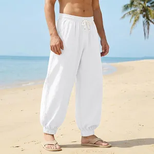 Men's loose white linen beach pants featured in a sunny tropical coastal setting