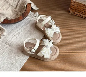 Gros plan de sandales crème pour filles avec nœuds en dentelle et fleurs en strass