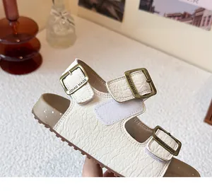 Gros plan sur une sandale pour enfant en cuir blanc avec boucles en bronze réglables