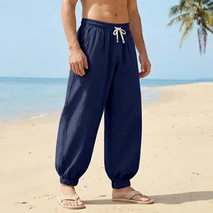 Men's lightweight loose linen jogger pants in navy blue shown in a sunny beach setting