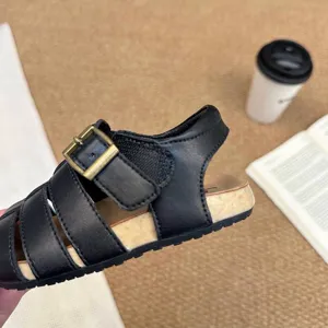 Primer plano de sandalia romana de cuero negro para niños con hebilla vintage y suela corcho.