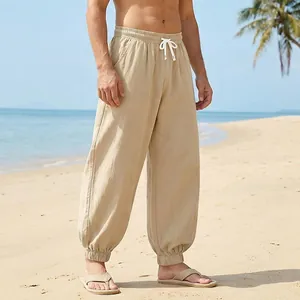 Full view of men's beige linen joggers on beach, showing loose fit and elastic cuff