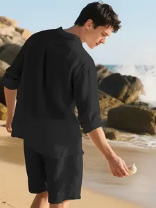 Rückansicht eines Mannes im schwarzen Leinen-Set mit Hemd und Shorts an einem Strand.