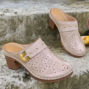 Macro view of beige closed-toe clogs with floral laser-cut patterns and gold buckle