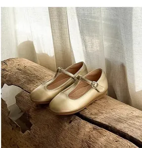 Retro champagne gold T-strap Mary Jane shoes for girls displayed on a rustic wood log