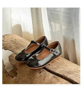 Detail view of black patent leather girls' T-strap Mary Jane flats displayed on a rustic wood log