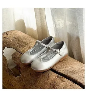 Detailed close-up of silver T-strap Mary Jane leather shoes for girls on a natural wooden log