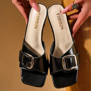Close-up of black square toe mule sandals featuring a stylish metal buckle detail.