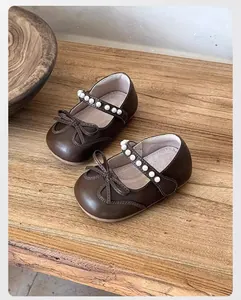 Detalle de los zapatos Mary Jane marrones para niños con elegante tira de perlas y lazo