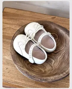 Vista detallada de zapatos de princesa blancos para niñas con lazo y perlas sobre madera