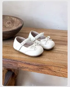 Vista detallada de zapatos blancos para niñas con correas de perlas y lazos