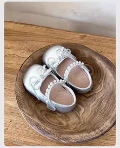 Zapatos plateados de princesa para bebé con lazo y correa de perlas en fondo de madera