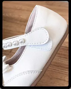 Primer plano de zapatos de princesa blancos para niña con correa de perlas y velcro