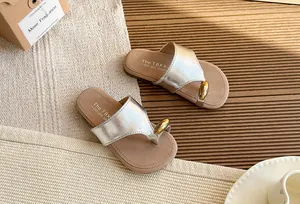 Detalle de la tira plateada metalizada y cuenta dorada en sandalias de dedo estilo