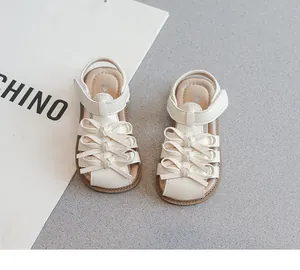 Nahaufnahme von cremefarbenen Kindersandalen mit süßen Schleifen und Klettverschluss