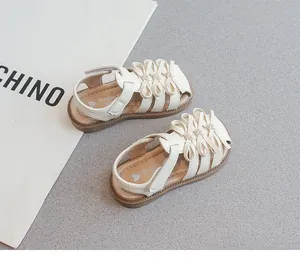 Detailansicht cremefarbener Mädchensandalen mit Schleifen auf strukturierter Fläche.