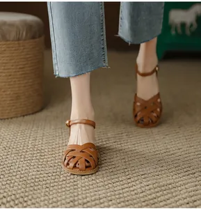Detail shot of French vintage brown woven leather sandals worn with denim jeans on a rug.