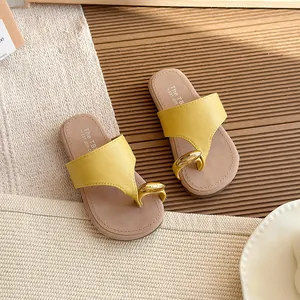 Sandalias de dedo amarillas para mujer con detalle de anillo dorado sobre fondo cálido