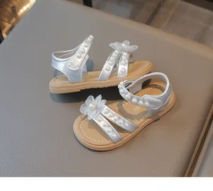 Detailansicht von silbernen Mädchensandalen mit Perlen und zarten Stoffblumenakzenten.