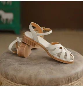Detailed side view of off-white woven leather sandals with ankle straps on a vintage stool