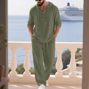 Mann in olivgrünem Leinen-Set mit Kapuze auf einem Balkon mit Blick auf das Meer