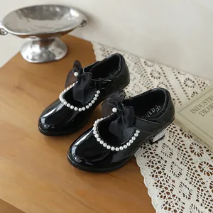 Close-up of black patent leather girls' shoes with pearl trim and mesh bow detail