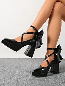 Elegant black patent leather platform pumps featuring a large bow and cross ankle straps