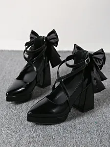 Close-up side view of black patent leather chunky high heels with large satin bows