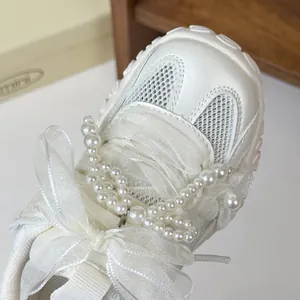 Dettaglio scarpe da ginnastica bianche per bambina con perle e fiocco di pizzo