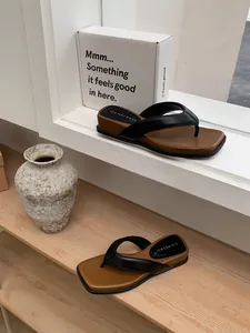 Tongs noires élégantes à semelle épaisse marron sur une étagère minimaliste chic.